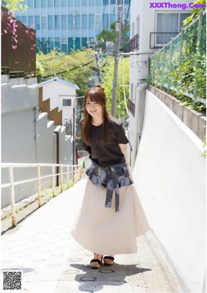 A woman in a black shirt and a beige skirt is walking down a sidewalk.