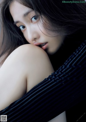 A woman in a black bodysuit sitting on a bed.