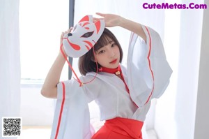 A woman in a red and white kimono sitting on a bed.