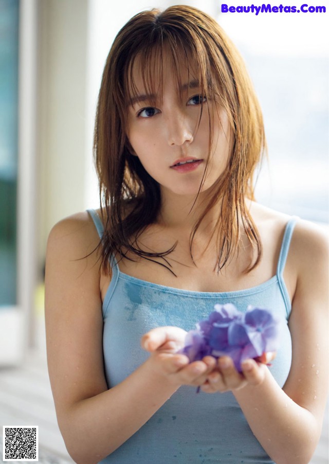 A woman in a blue tank top holding a purple flower.