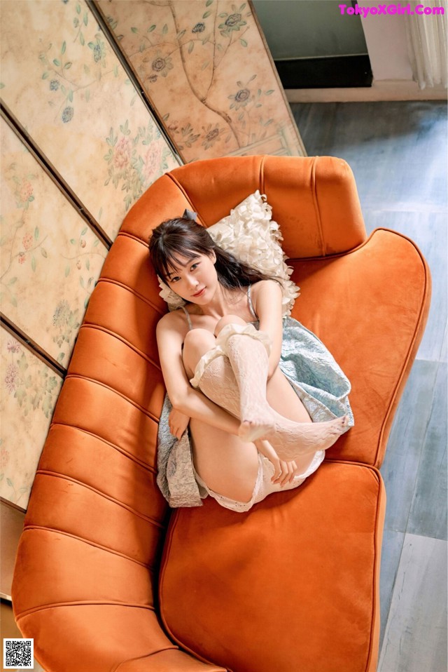 A woman laying on top of an orange couch.