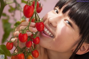 A young girl holding a cherry in front of her face.