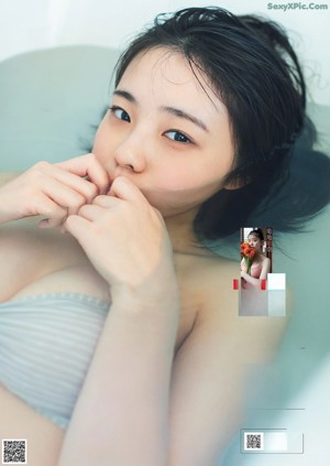 A woman in a pink bikini top and shorts leaning against a blue wall.