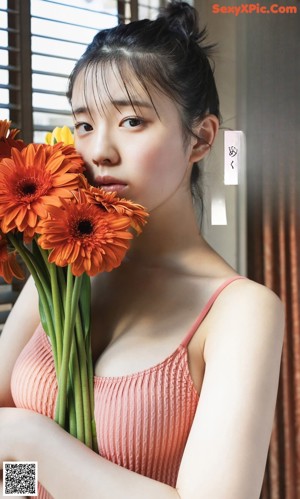 A woman in a bathing suit holding a bunch of flowers.