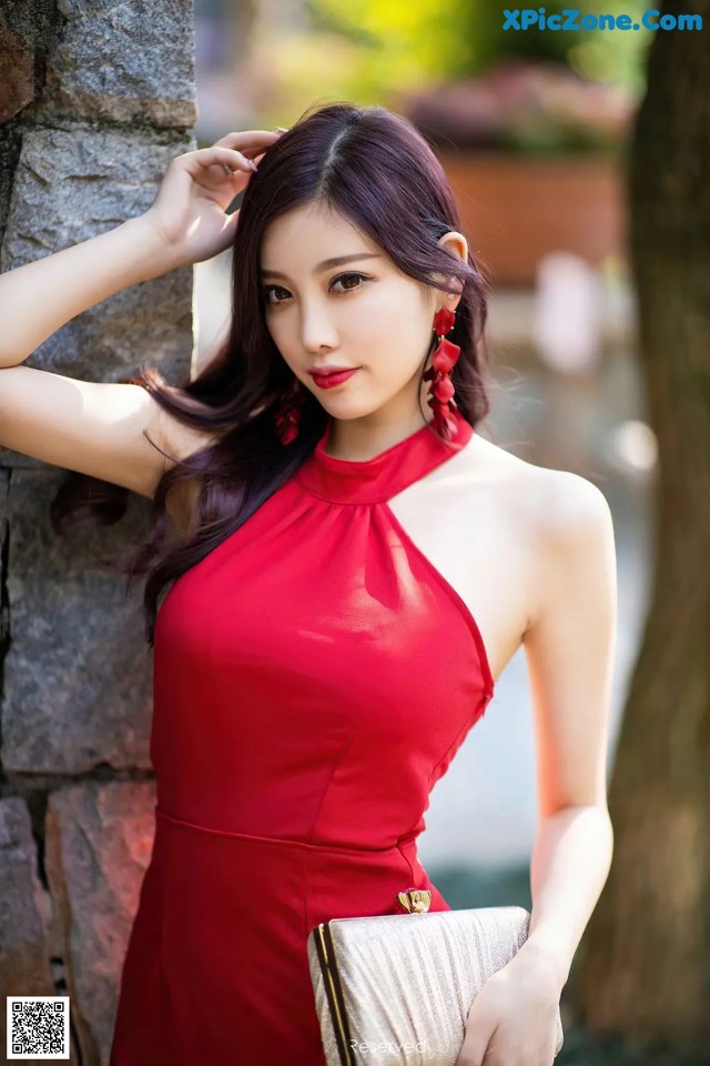 A woman in a red dress leaning against a stone wall.