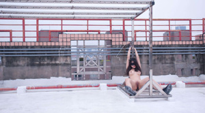 A naked asian woman is tied up and tied up to a pole.