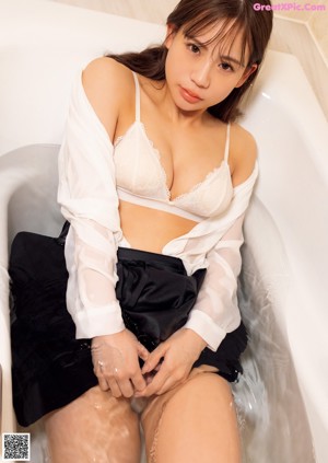 A woman in a white bra sitting in a bathtub.