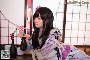 A woman in a kimono sitting on the floor next to a lamp.