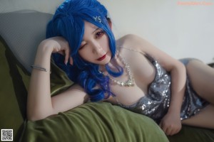 A woman with blue hair sitting on a bed.