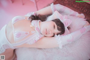 A woman in a white lingerie posing in front of a pink wall.