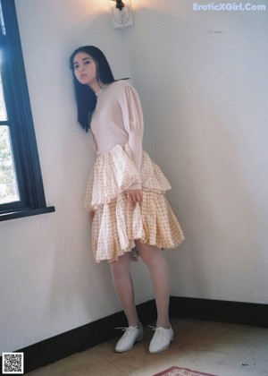 A woman with long black hair leaning against a wall.