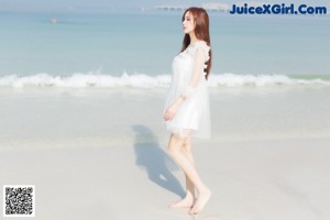 A woman in a white dress sitting on a beach.