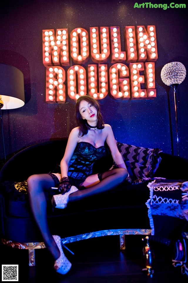 A woman sitting on a couch in front of a neon sign.