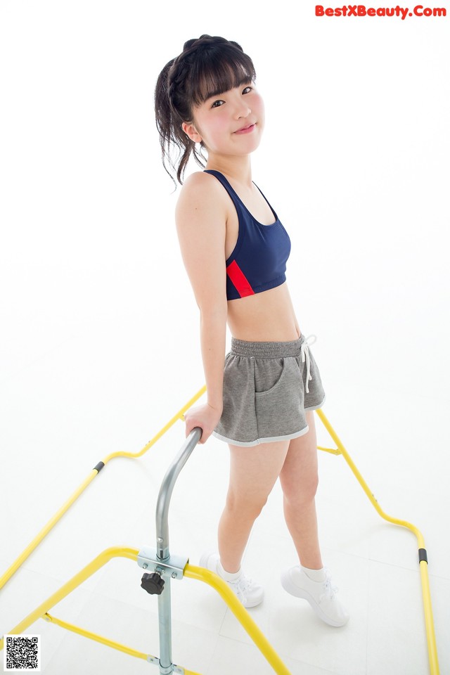 A young woman in a blue sports bra top and gray shorts.