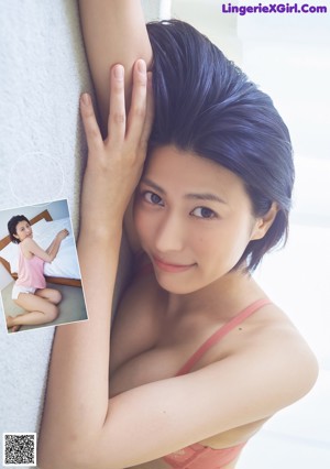 A woman sitting on a bed in a pink top and white shorts.