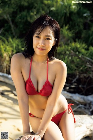 A woman in a red bikini sitting on a rock.